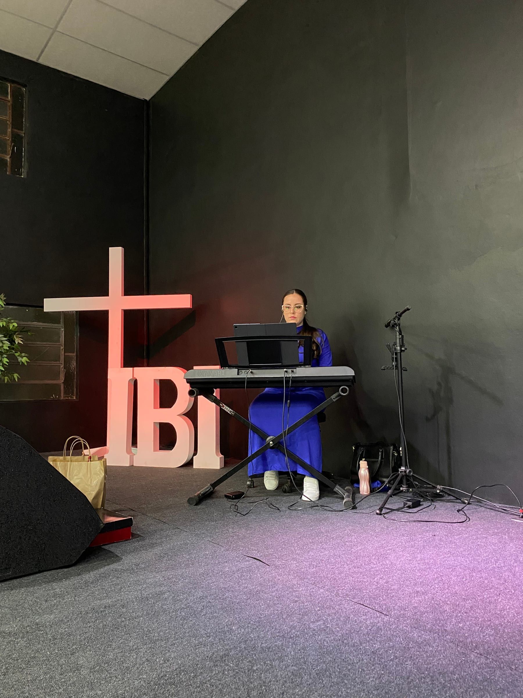 Cruz de madeira e as letras IBI iluminadas no palco da igreja.