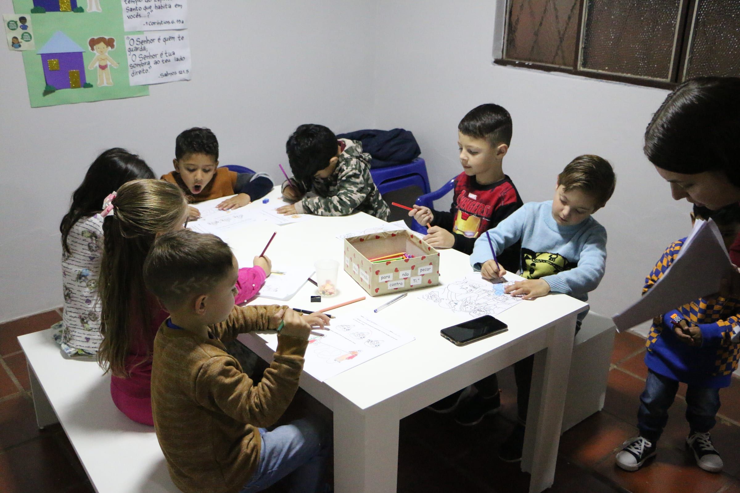 Crianças desenhando em volta de uma mesa na escolinha bíblica.